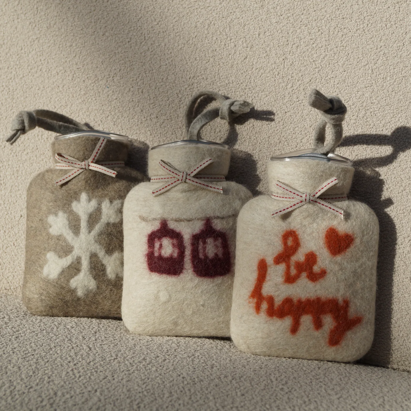 Three hand-felted alpine hot water bottles — snowflake, gondolas and 'be happy' embroidery