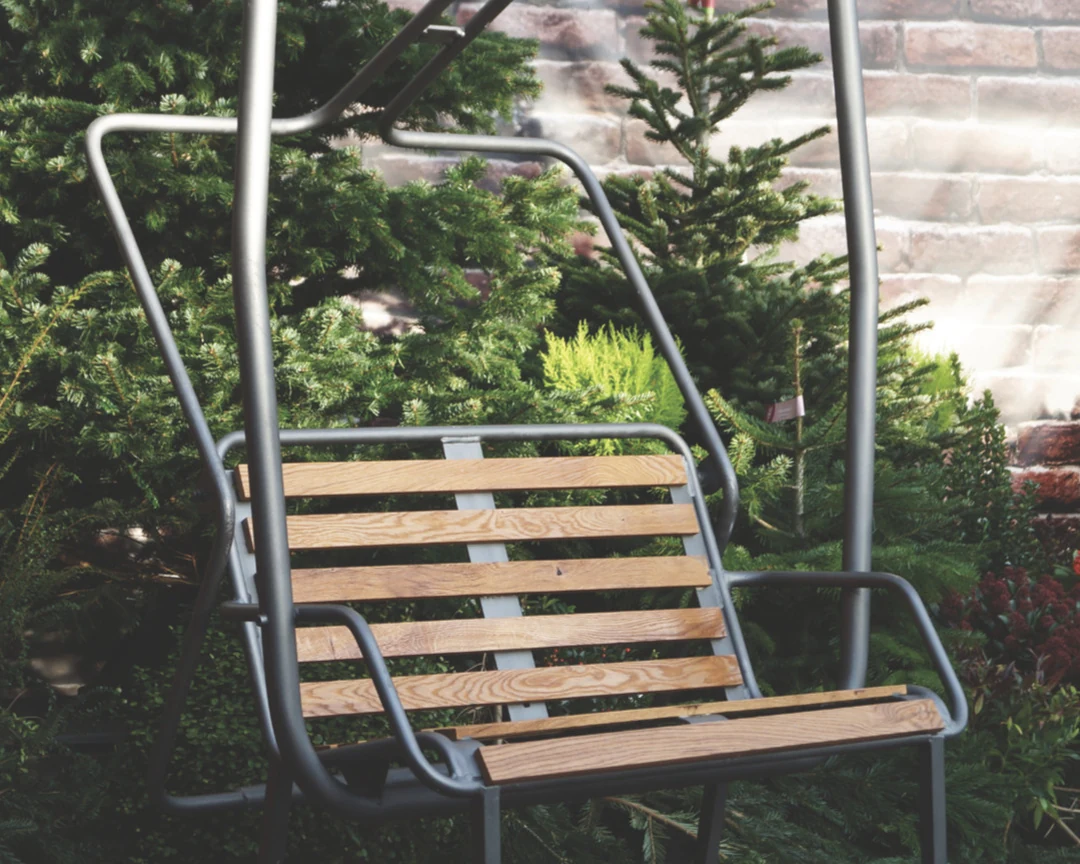 Dzorniva chairlift bench — steel and oak, set against fir trees and a brick wall