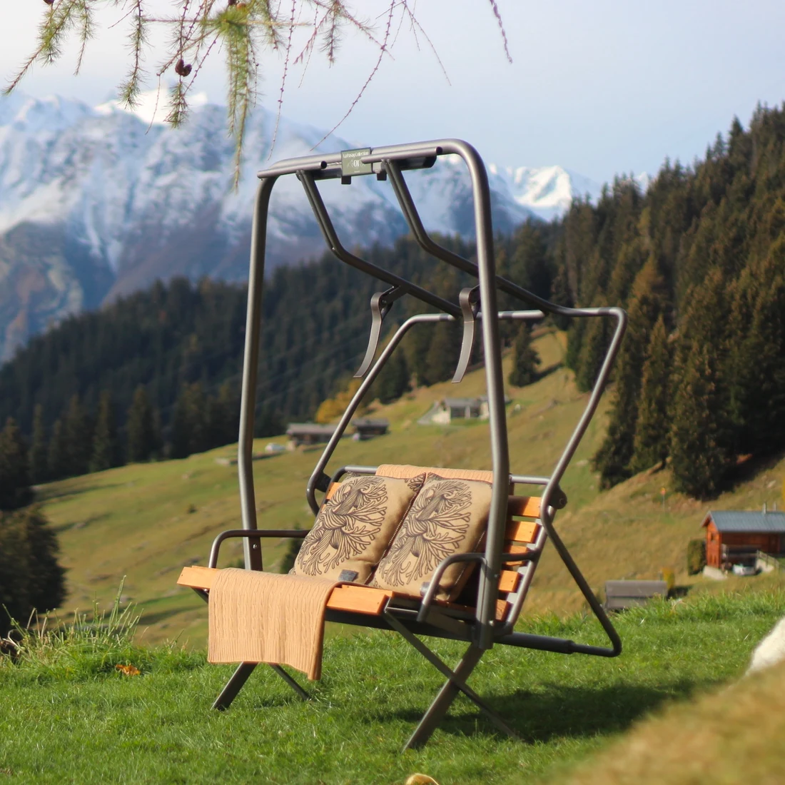 La Pasay chairlift refurbished as a numbered outdoor bench, set on a Bruson alpine meadow with snow-capped peaks behind