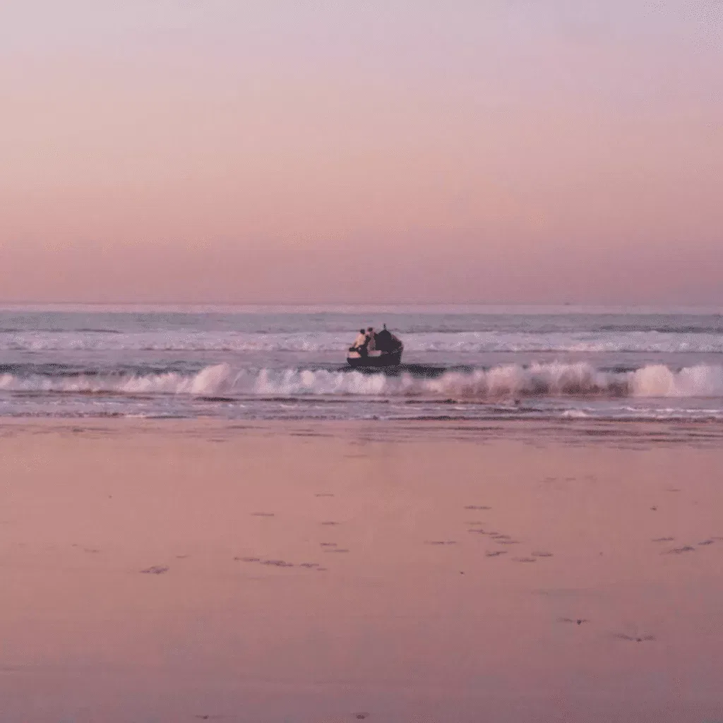 A small boat on the Moroccan coast at dusk, pink sky reflecting on wet sand