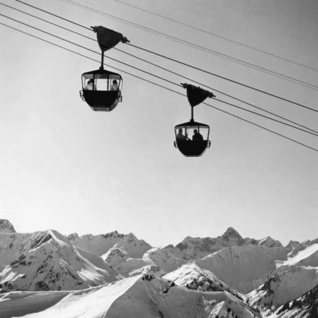 Black-and-white photo of vintage gondolas suspended above alpine peaks